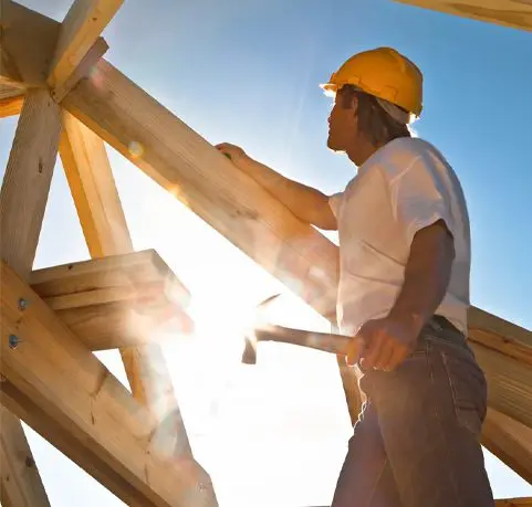 A man in yellow hard hat working on roof structure.