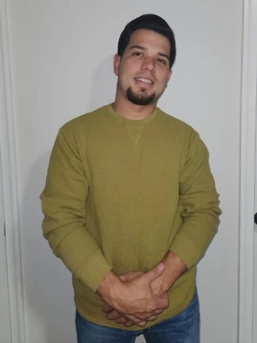 A man in a green shirt standing next to a white wall.